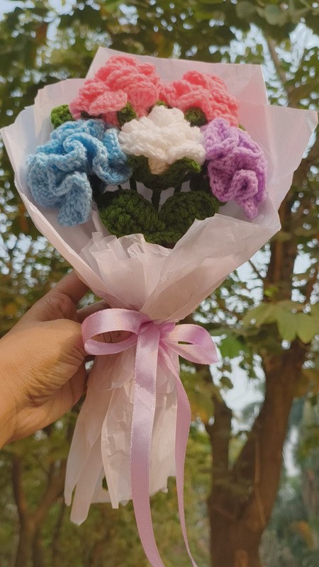 A bouquet of pink, blue, cream and purple crochet flowers tied with a ribbon